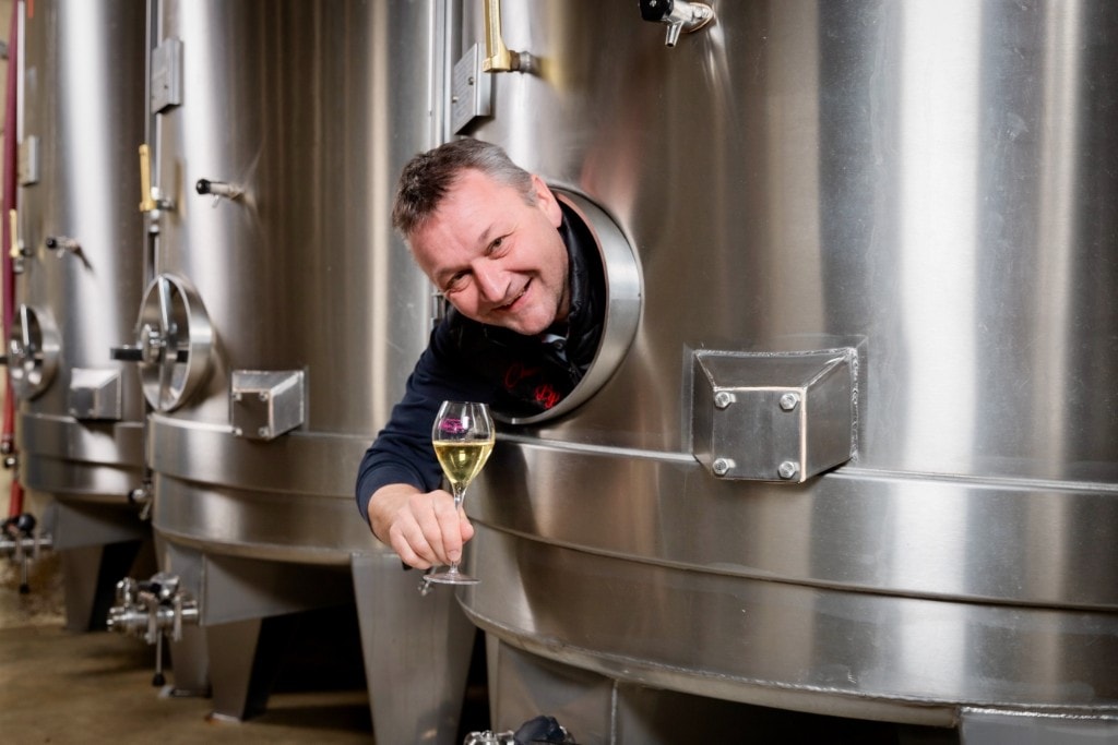 Michael Blaise dans la cuverie, verre de champagne à la main